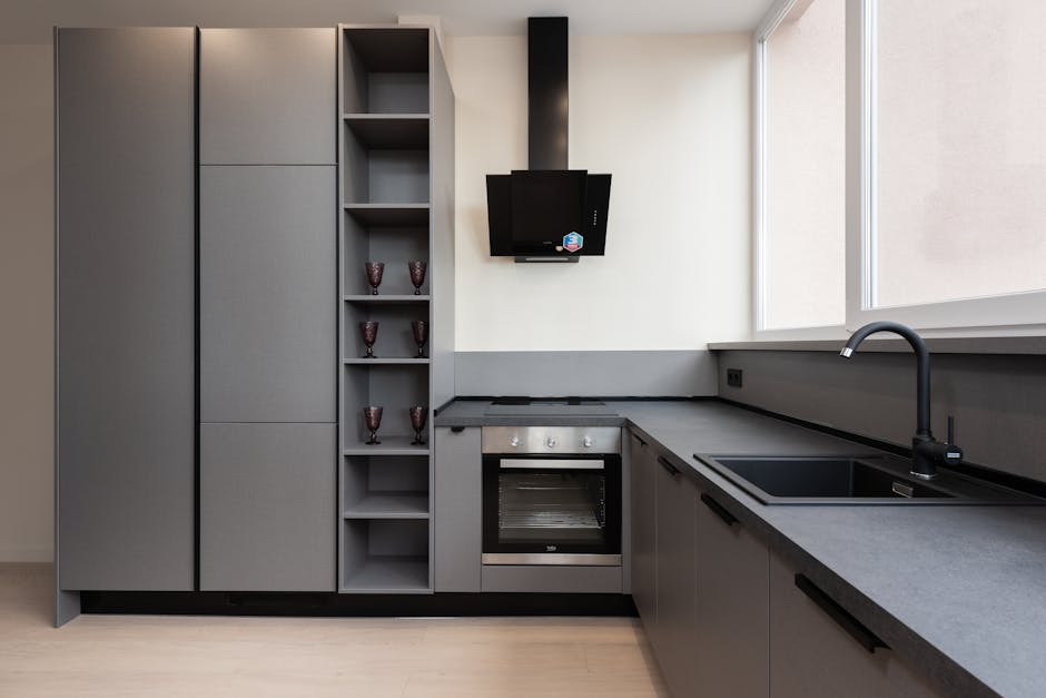 A modern kitchen featuring white cabinetry and a black marble backsplash with white veining. The black glass-ceramic cooktop is integrated into the black marble countertop, which appears clean and pol